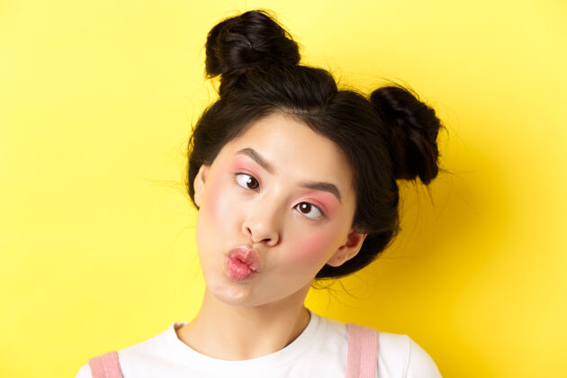 明亮有趣的亚洲少女的特写肖像 迷人的妆容和发型 眯着眼睛 傻傻地撅着嘴唇 站在黄色的舞台上女性真实惊人