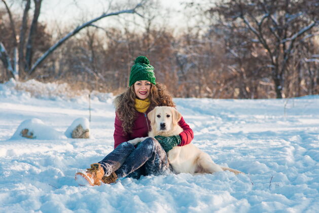 雪快乐美丽的年轻女子 在冬天的日子里 把手中的雪花吹给她的金毛猎犬狗手套休闲