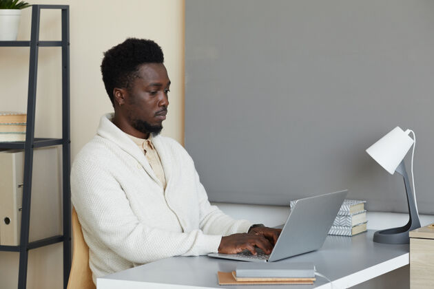 笔记本电脑坐在桌子旁专注于在线工作的非洲年轻人在办公室用笔记本电脑打字桌子自信商务人员