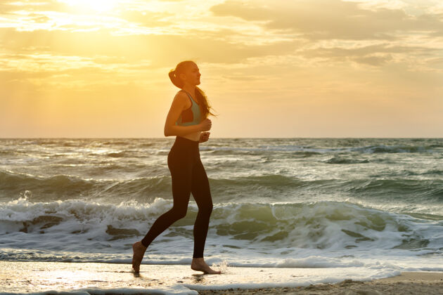 上衣穿着运动服的女孩沿着海浪奔跑行早早晨成人女性生活方式