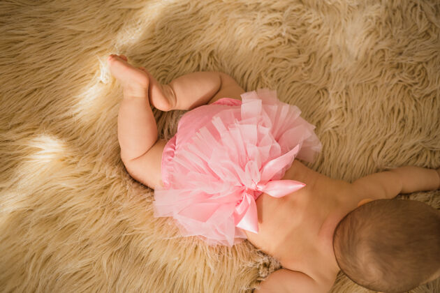 背部女婴的屁股在米色毛绒毯上穿着粉色褶边内裤褶边床爬行