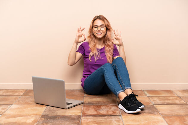 平衡一个女人拿着笔记本电脑坐在室内的地板上 摆出禅宗的姿势互联网护理学习
