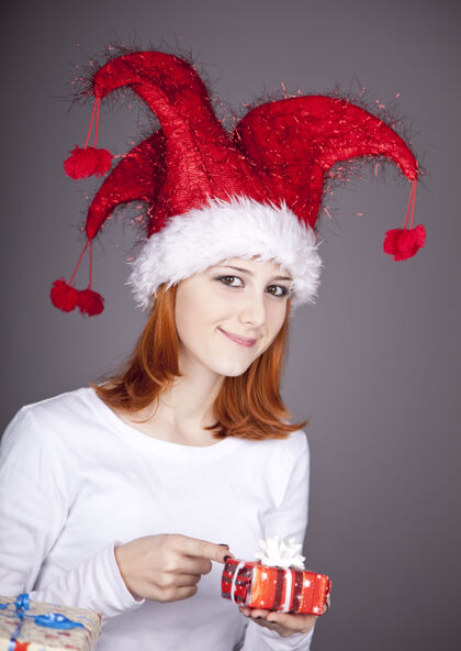 快乐滑稽的红发女孩戴着圣诞帽 手里拿着礼品盒盒子女士包装