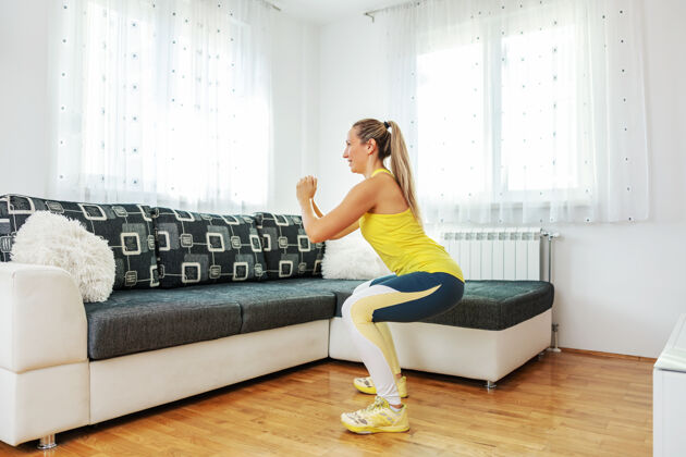 臀部微笑健康的女运动员做蹲在家里形状减肥室内