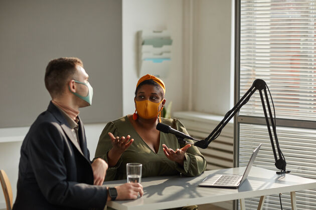 戴着防护面具的商界人士坐在餐桌旁 在电台直播中讨论世界形势防护面罩工作人员