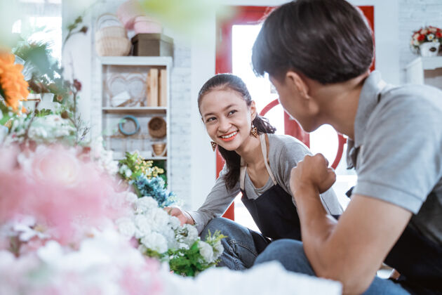 男人一对穿着围裙的年轻夫妇在花店工作时微笑着交谈商业生活方式卖家