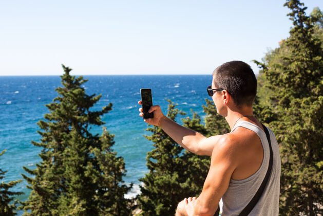 背包男游客用智能手机拍摄山区美丽的海景男性自由远足