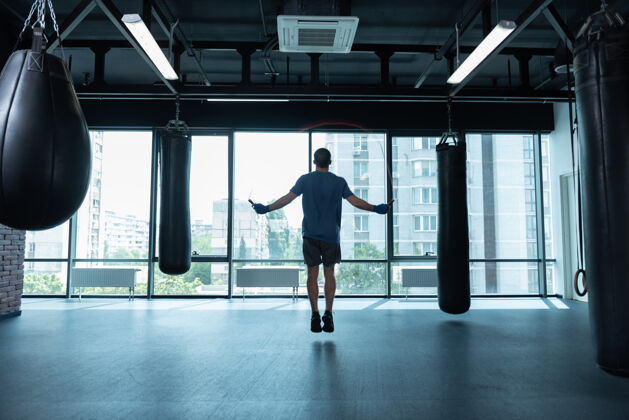运动跳绳穿着蓝色衬衫的黑发运动员站在窗外跳绳 可以看到城市的景色拳击手套教练压力