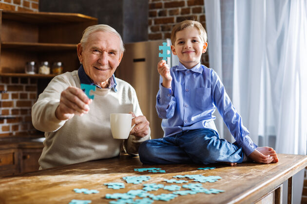 表情快乐的老人和他可爱的小孙子在厨房里拼图孙子小学习
