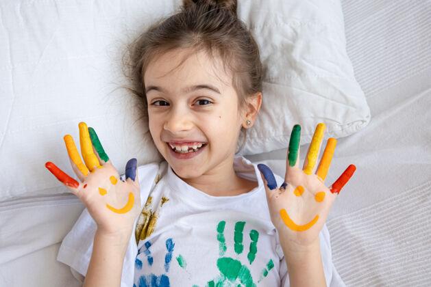 凌乱一个穿着印有彩色手印的t恤的小女孩的手掌上画着微笑微笑乐趣艺术品