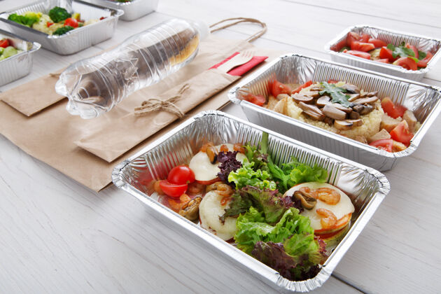 食物用铝箔盒带走食物蔬菜 生菜和芝士配虾仁 纸袋和水瓶在白木容器水送货