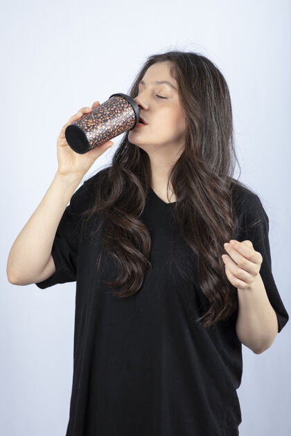 姿势一位留着长发的黑发女人从杯子里喝水的照片站立咖啡女性