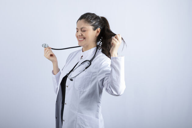 医疗保健穿着白大褂的漂亮女医生在白墙上摆好听诊器的姿势黑发听诊器职业
