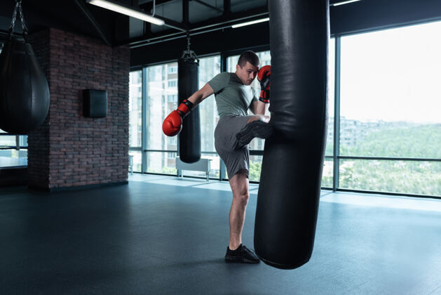 运动站起来黑发职业经验丰富的拳击手一边用腿打拳击袋一边刻苦训练动机男性压力