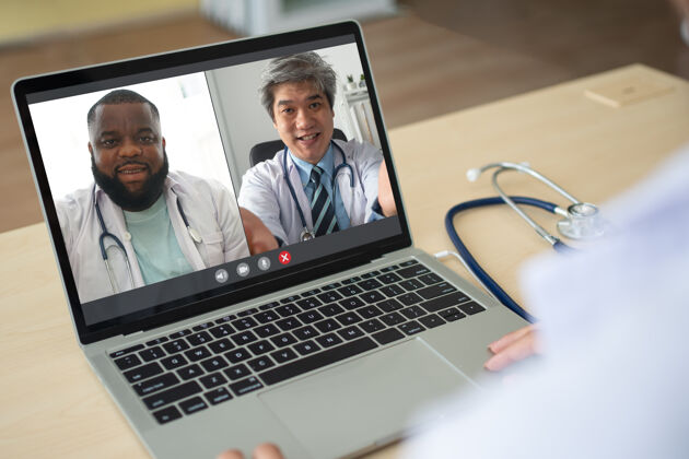 亚洲亚裔资深医生和非裔美国人颈部戴白大衣听诊器的屏幕应用视图和视频会议 讨论和分享如何治疗该病病毒概念远程医疗屏幕网络摄像头医疗