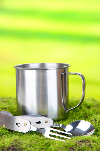 咖啡金属杯 勺子和叉子放在绿草上 放在大自然上勺子马克杯闪亮