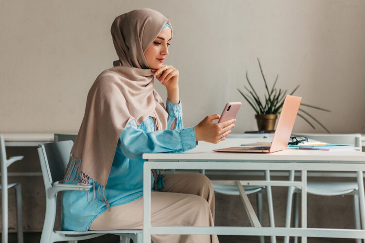 移动年轻漂亮的现代妇女戴着头巾在办公室的笔记本电脑上工作 教育在线教育民族电话