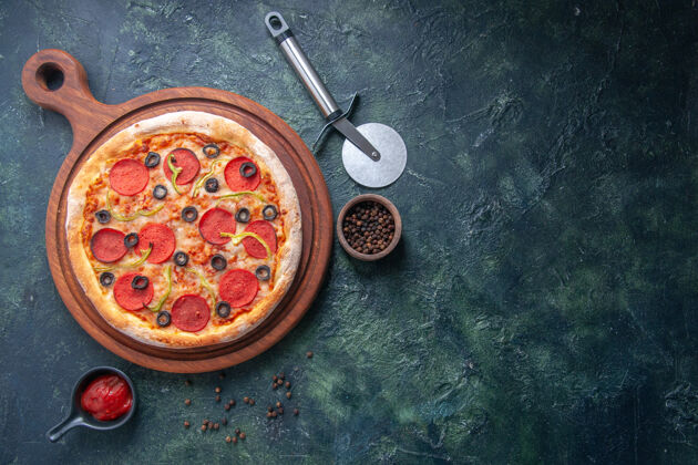 营养品美味的比萨饼放在木制的砧板上 胡椒番茄酱放在右边 在孤立的黑暗表面上蔬菜美味比萨饼餐