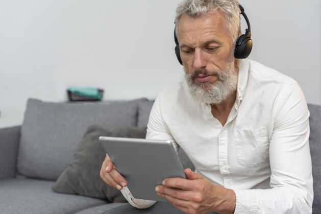 房子家里的老人在沙发上用平板电脑和耳机平板电脑胡须老年人