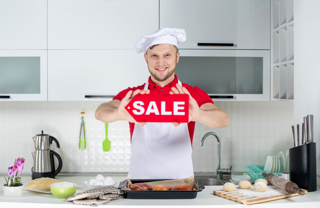 观点白色厨房里年轻微笑的男厨师展示销售标志的俯视图微笑房子专业