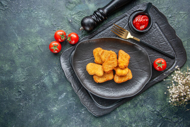 水果黑色盘子上的鸡块和优雅的叉子番茄酱在深色托盘上白色的花番茄托盘花午餐