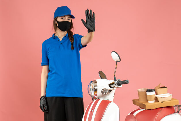背景顶视图自信的信使女孩戴着医用口罩手套站在摩托车旁边 上面有咖啡蛋糕 在柔和的桃色背景上显示五个手套显示穿