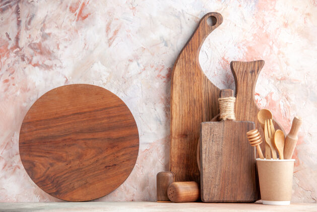 烹饪不同尺寸和形状的棕色木砧板正面图 站在彩色表面的墙上景观餐具勺子