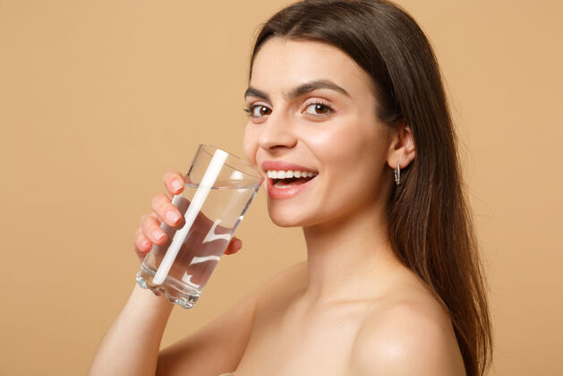 皮肤特写黑发半裸完美皮肤的女人裸妆玻璃水隔离米色粉彩墙健康饮食口渴