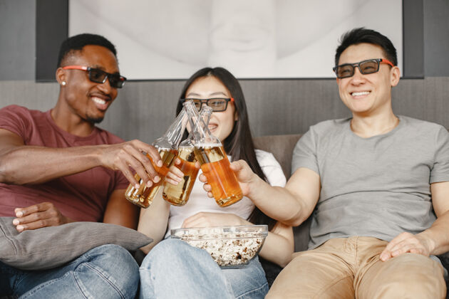 非洲一对非洲男孩和一对亚洲夫妇和一对看电影的朋友碰杯喝啤酒 戴着眼镜吃爆米花看电影聚会电影爆米花