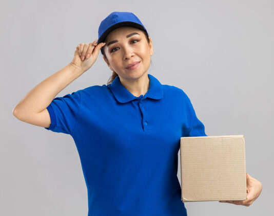 微笑快乐的年轻送货员身穿蓝色制服 头戴鸭舌帽 面带微笑地站在白色的墙上交货立场举行