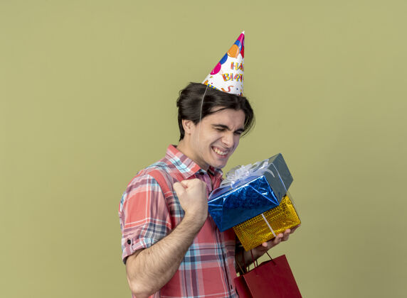 纸高加索帅哥戴着生日帽 手里攥着礼品盒和购物袋兴奋绿色橄榄