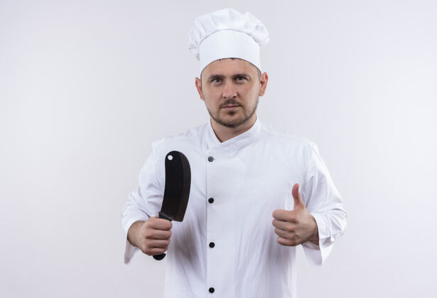 烹饪自信的年轻帅哥厨师身着厨师制服手持菜刀 在与世隔绝的白墙上竖起大拇指菜刀秀年轻