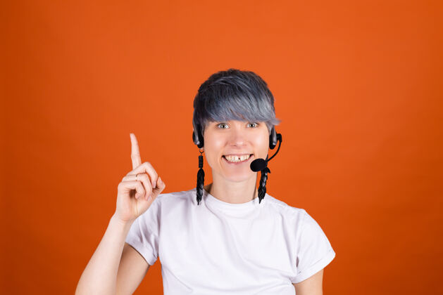 女性电话中心助理戴着耳机站在橙色的墙上 看起来很开心 充满自信的微笑 手指朝上耳机接线员耳机