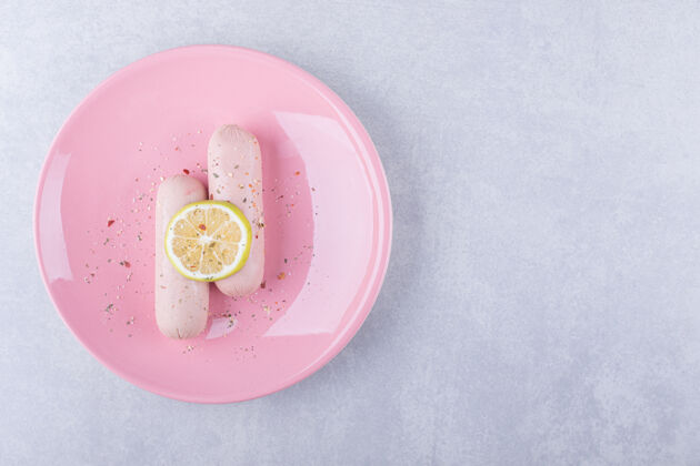美味粉红色盘子上装饰着柠檬的煮香肠烹饪晚餐食物