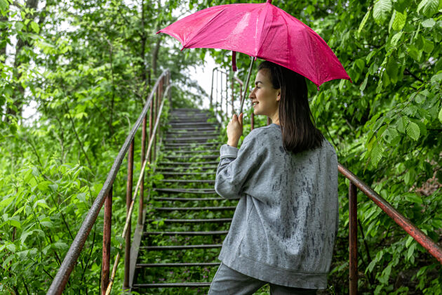 乡村女孩在雨中打着伞在春天的森林里散步下雨草风景