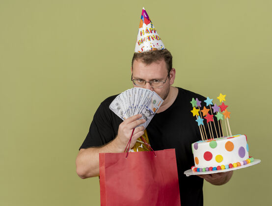 人自信的成年斯拉夫人戴着眼镜 戴着生日帽 手里拿着钱 纸 购物袋和生日蛋糕信心购物成人