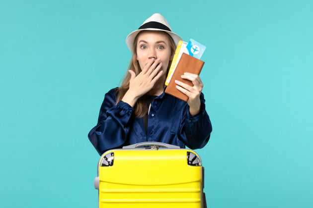 旅行正面图年轻女子拿着机票 准备在蓝底旅行海上度假旅行飞机旅行美丽准备微笑