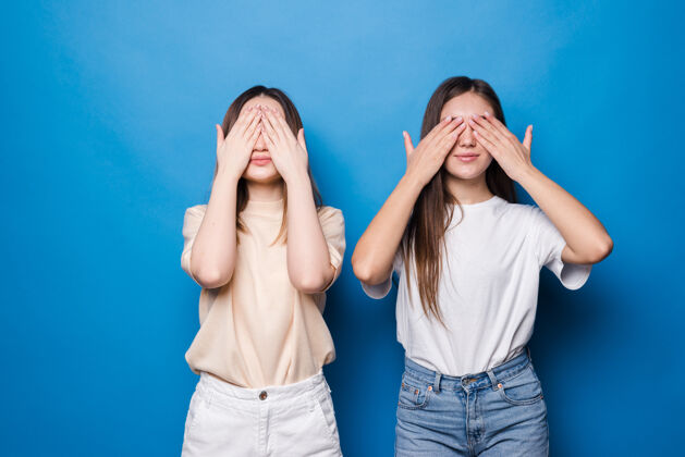 快乐年轻女孩用手遮住眼睛 隔离在蓝色的墙上夫妇女人花