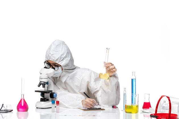 人员正面图身着特殊防护服的年轻女化学家拿着装有溶液的烧瓶 在白色背景上用显微镜观察实验室的病毒化学防护实验室外套医生