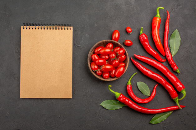 辣椒顶视图：红辣椒 荷叶 一碗樱桃西红柿和一本笔记本放在黑桌子上烹饪辣椒番茄