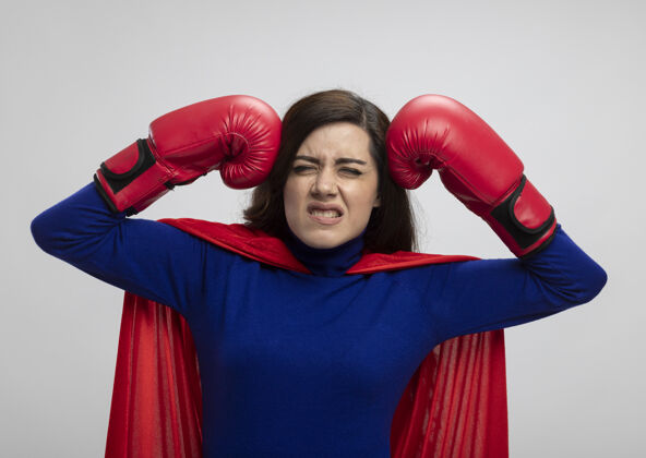 斗篷恼怒的高加索超级英雄女孩穿着红色斗篷戴拳击手套把拳头放在头上拳击拳头手套