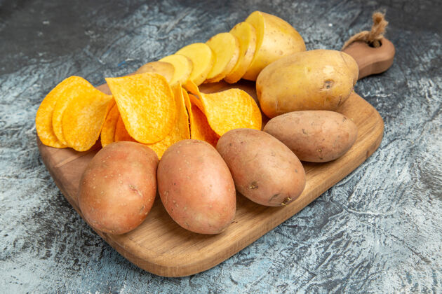 杏灰色背景的木质砧板上的脆片和生土豆的俯视图木材食品营养