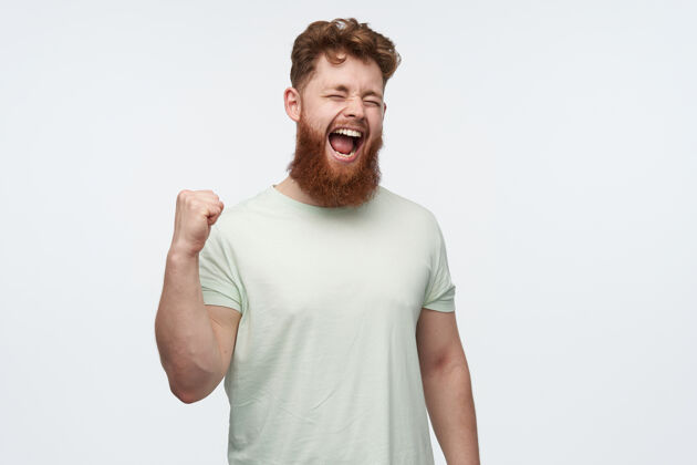 休闲年轻的红胡子男人的画像穿着一件空白的t恤 举起拳头 一边看足球比赛一边大喊大叫男人时尚模特