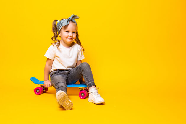 人时尚的小女孩穿着休闲装 在黄色的墙上玩滑板人快乐女孩
