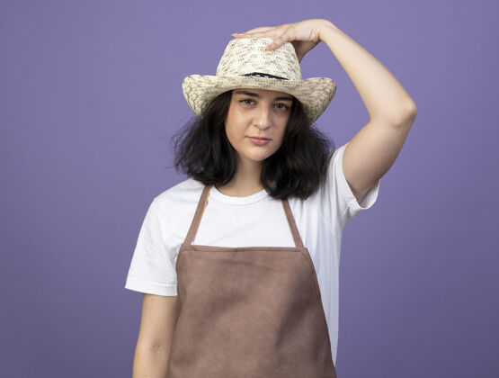 女人自信的年轻黑发女园丁身着制服 手戴紫墙上隔离的园艺帽自信女人花园