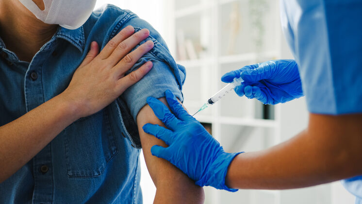 医院年轻的亚洲女护士给老年男性病人注射covid-19或流感病毒疫苗手套治疗访问