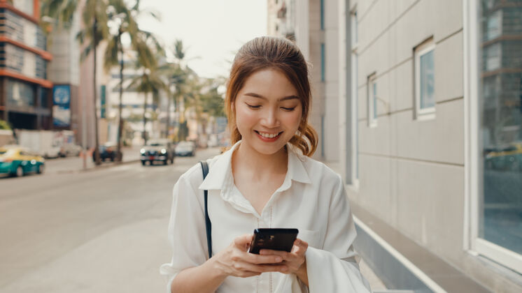 街道成功的亚洲年轻女商人穿着时尚的办公服 使用智能手机和打字短信专业人士女性户外