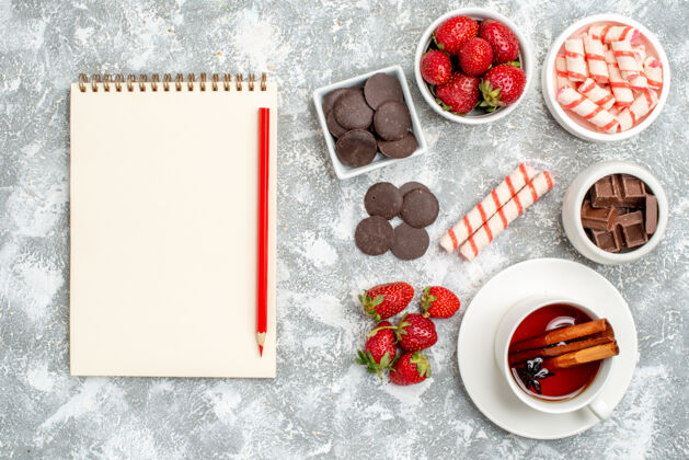 鲜花顶视图碗草莓巧克力糖果桂皮茴香籽茶和笔记本与铅笔在灰白色的地面甜点肉桂水果
