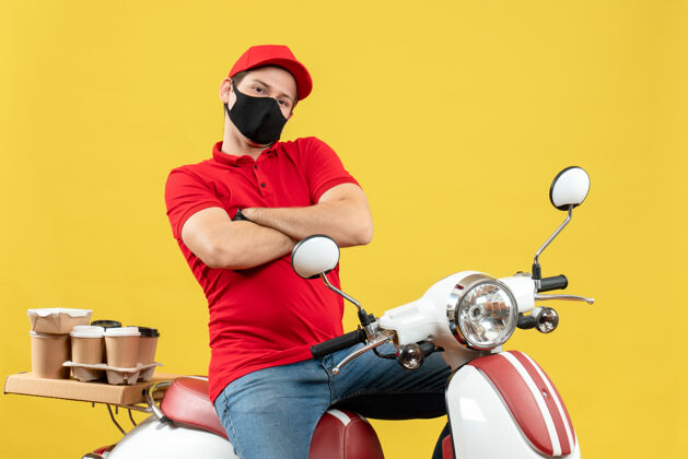 医疗俯视图：穿着红色上衣 戴着帽子 戴着手套 戴着医用面罩 坐在黄色背景的踏板车上传递命令的年轻人车辆男子命令