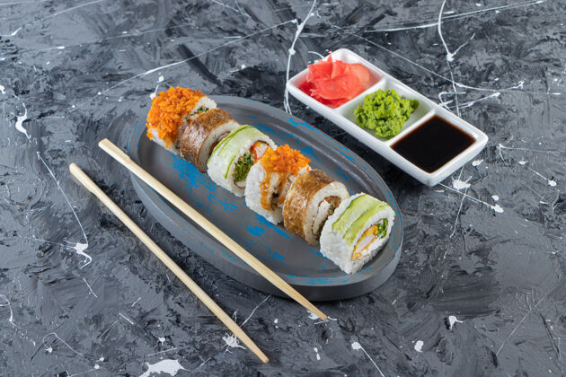 什锦大理石背景上各种寿司卷的蓝色盘子蟹筷子晚餐